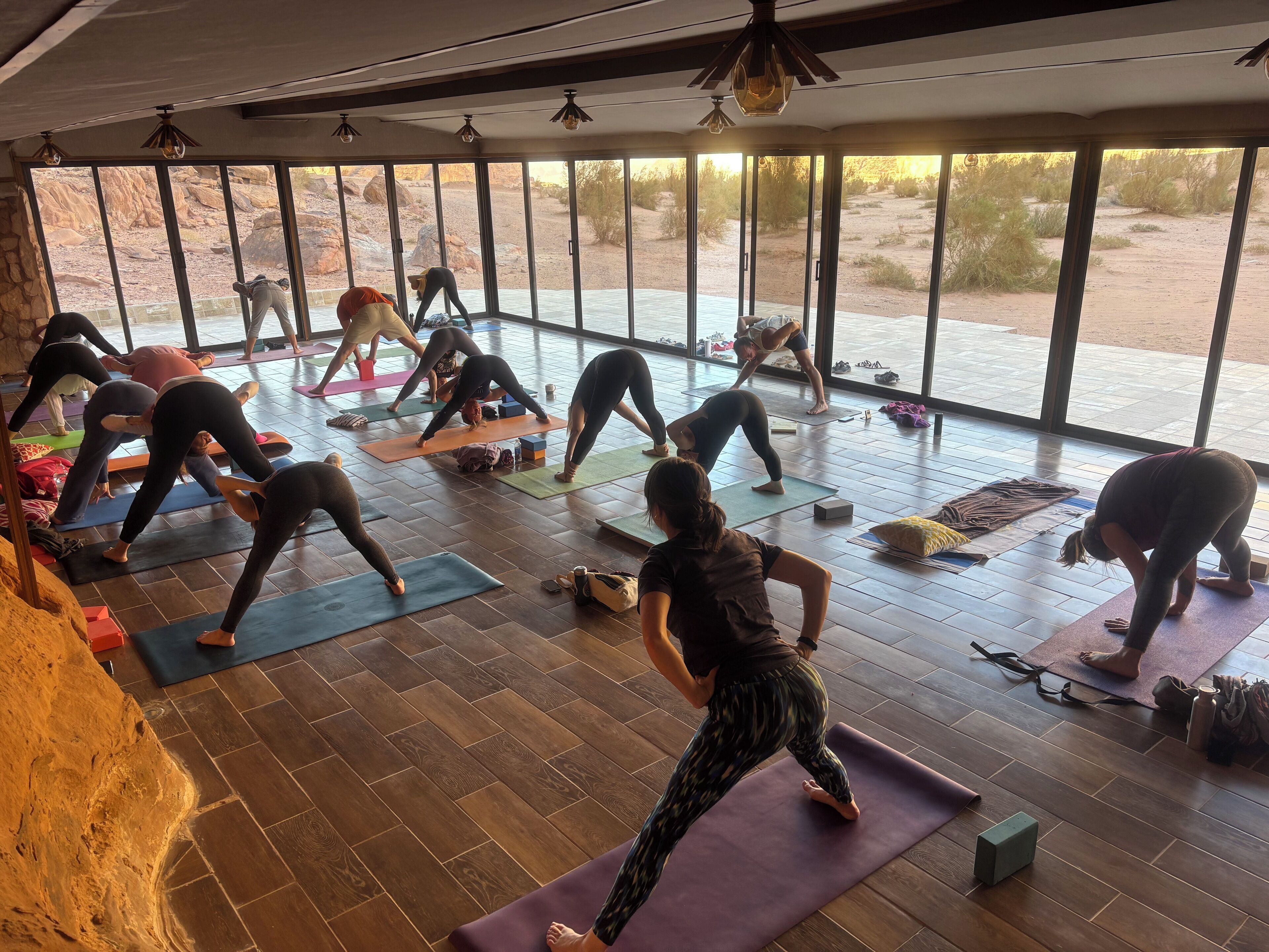 Ein Yoga-Kurs in einem Raum mit großen Fenstern, Holzdielen und Trainingsmatten.