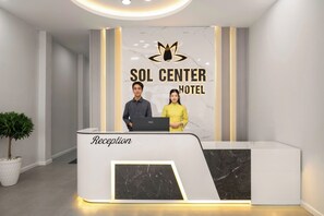 Mostrador de recepción en el Hotel Sol Center, con diseño moderno, una pared de mármol y un logotipo sobre el nombre.