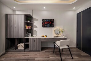 Una habitación moderna con un escritorio empotrado, una silla, un armario grande, un letrero de Netflix en la pared y una pequeña planta en maceta.
