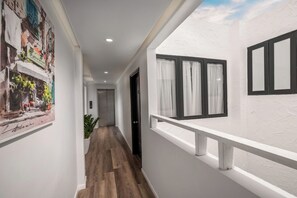 Un pasillo con suelo de madera, una puerta y una ventana con cortinas.