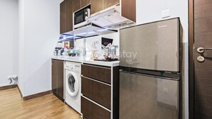 A compact kitchen with a washing machine, a refrigerator, and a microwave.