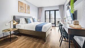 A modern hotel room with a bed, desk, and large window with a city view.