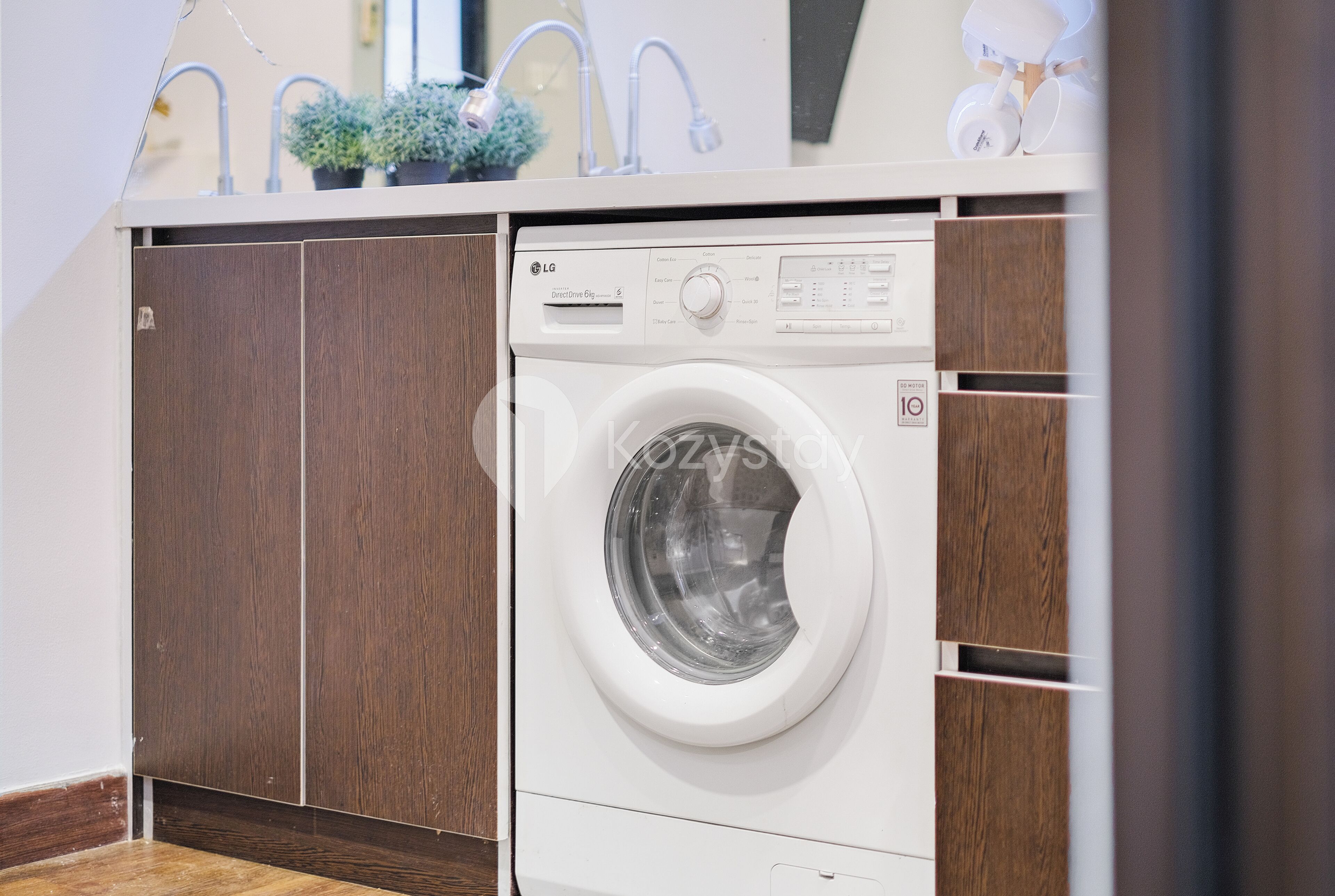 A front-loading washing machine in a compact, modern laundry room with wooden cabinetry and a countertop above.
