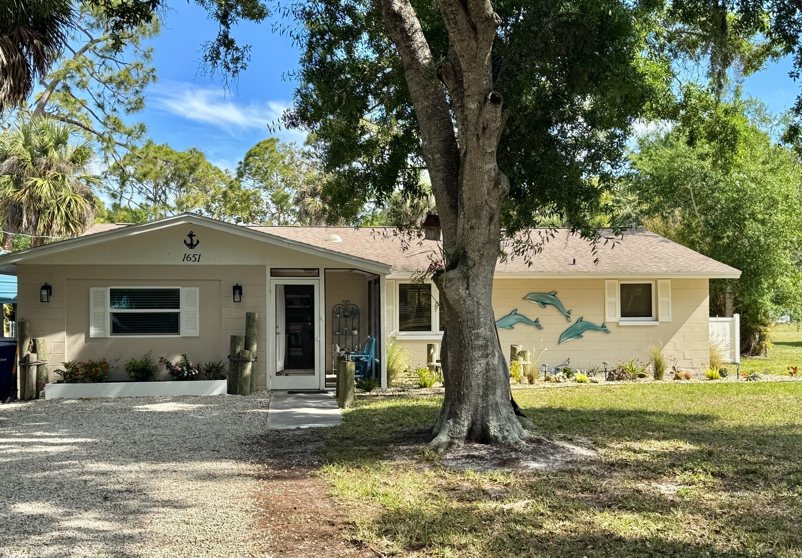 A house with a number 1651, a front porch, a tree, and a dolphin mural on the side.