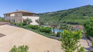 Una casa a due piani con piscina, immersa nel verde e circondata da colline.