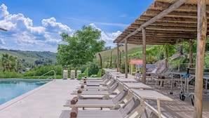 Un'area con piscina, lettini, una zona salotto coperta e vista sul paesaggio.