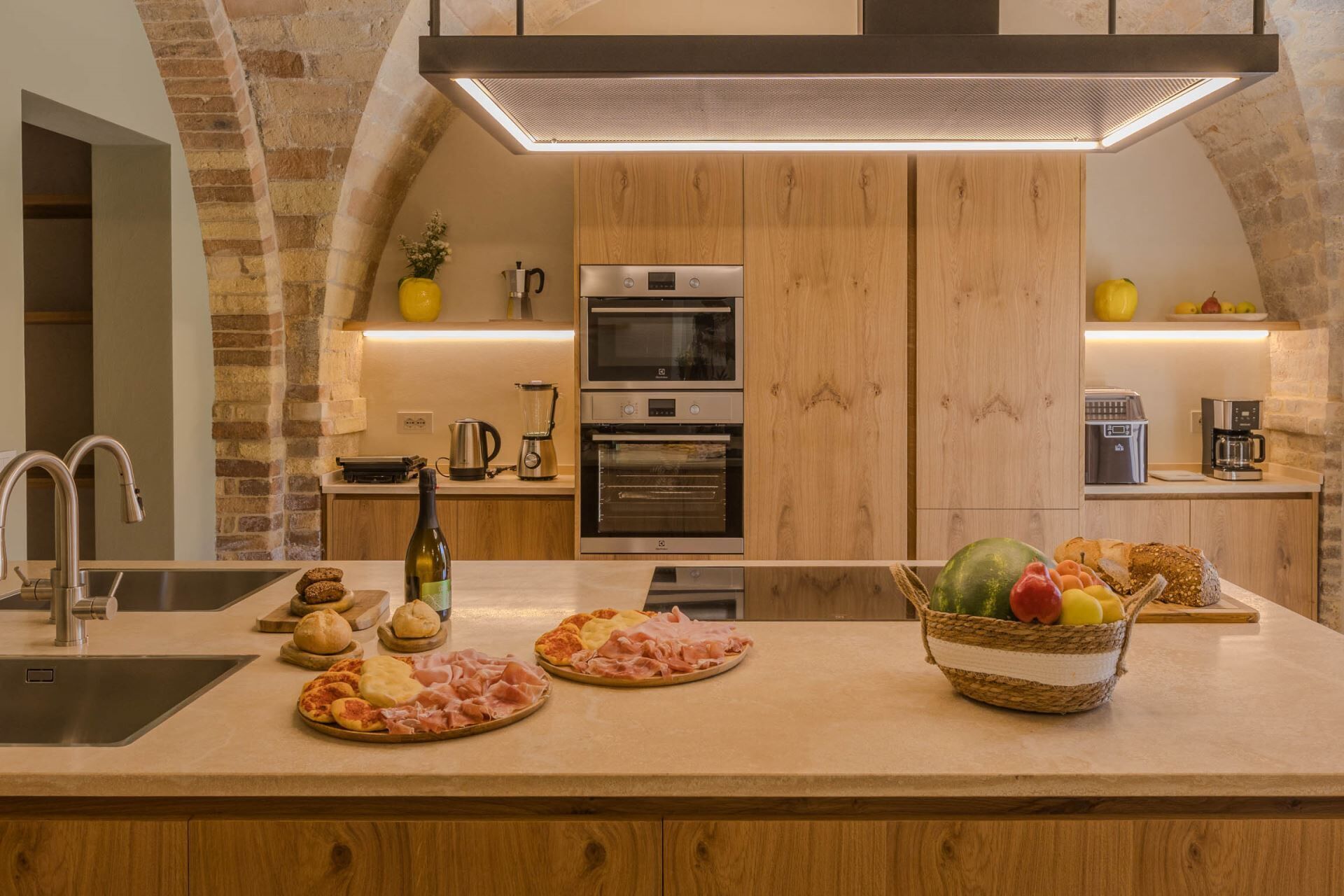 Una cocina moderna con una isla central, hornos integrados y una pared de acento de ladrillo.