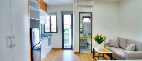A modern, compact living space with a kitchenette, a sofa, and a small table with a vase of flowers.