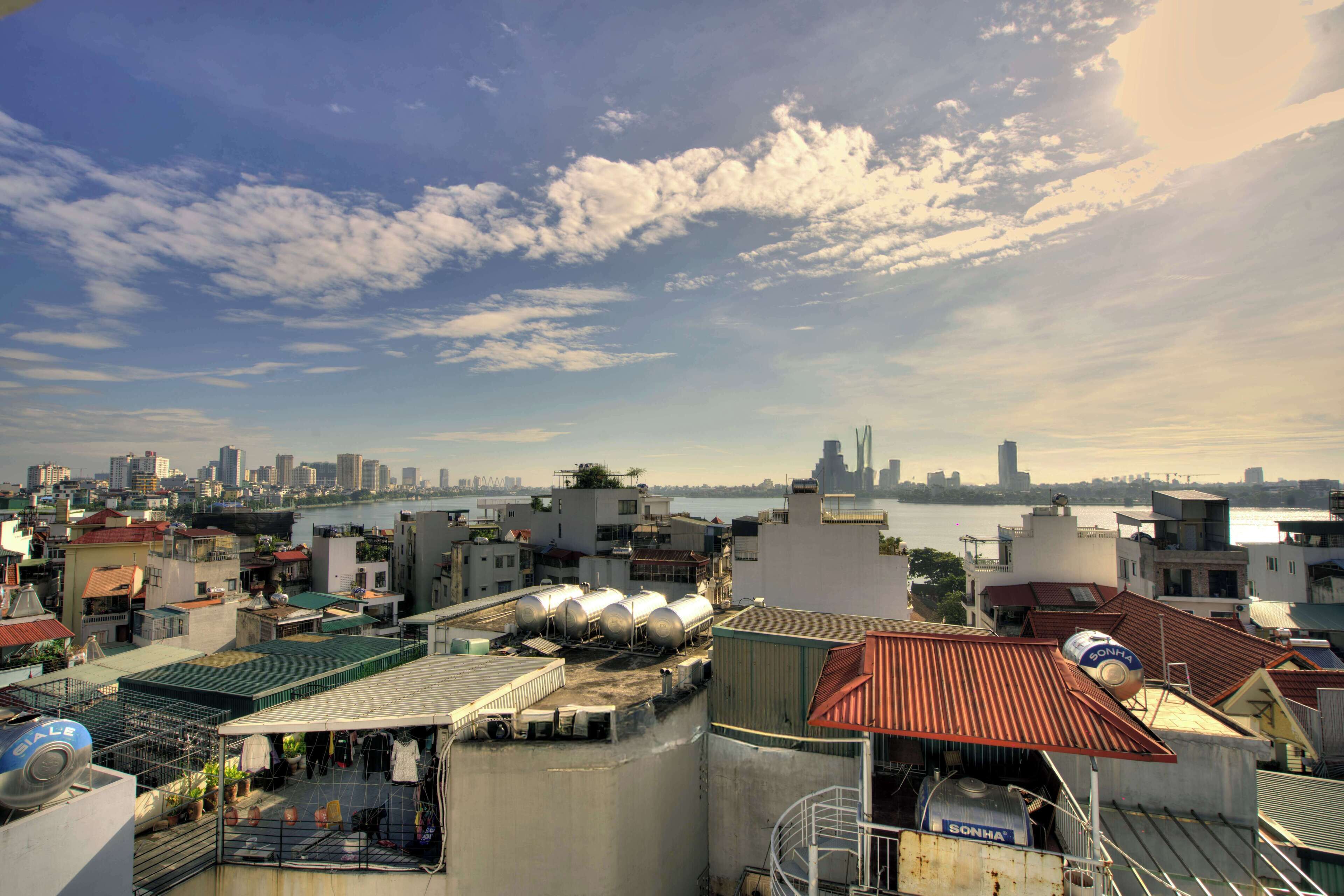 A rooftop with industrial tanks, a water body, and a city skyline in the background.
