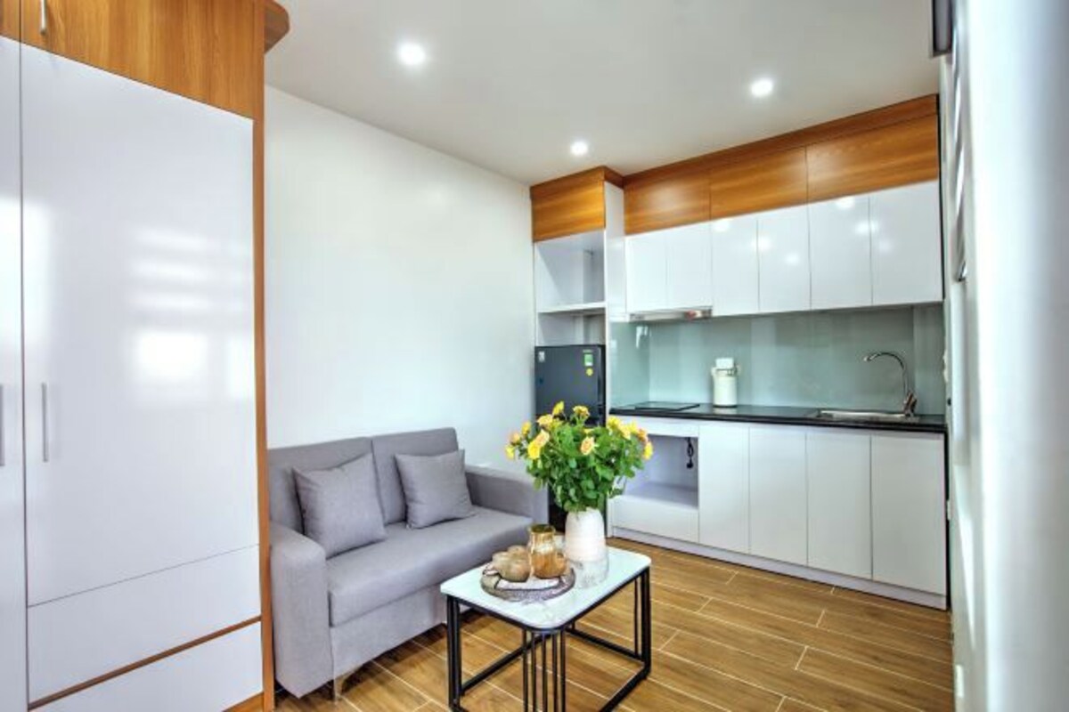 A modern kitchen with white cabinets, a grey sofa, and a small table with a vase of flowers.