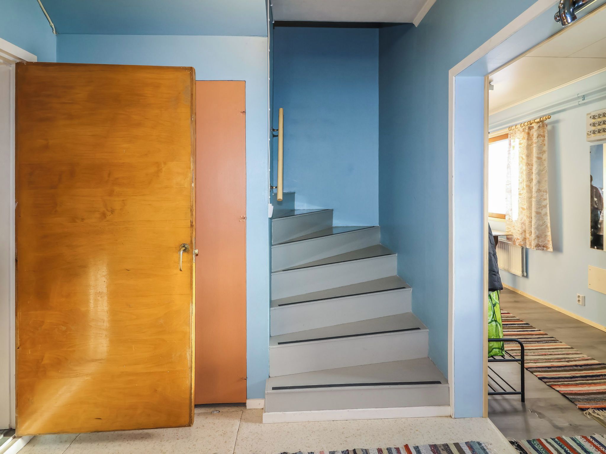 A staircase with a wooden door on the left and a hallway with a patterned rug on the right.