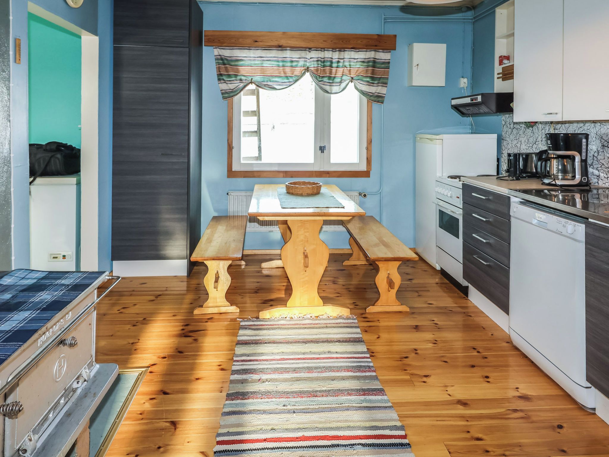A compact kitchen with a wooden table, a bench, and a striped rug.