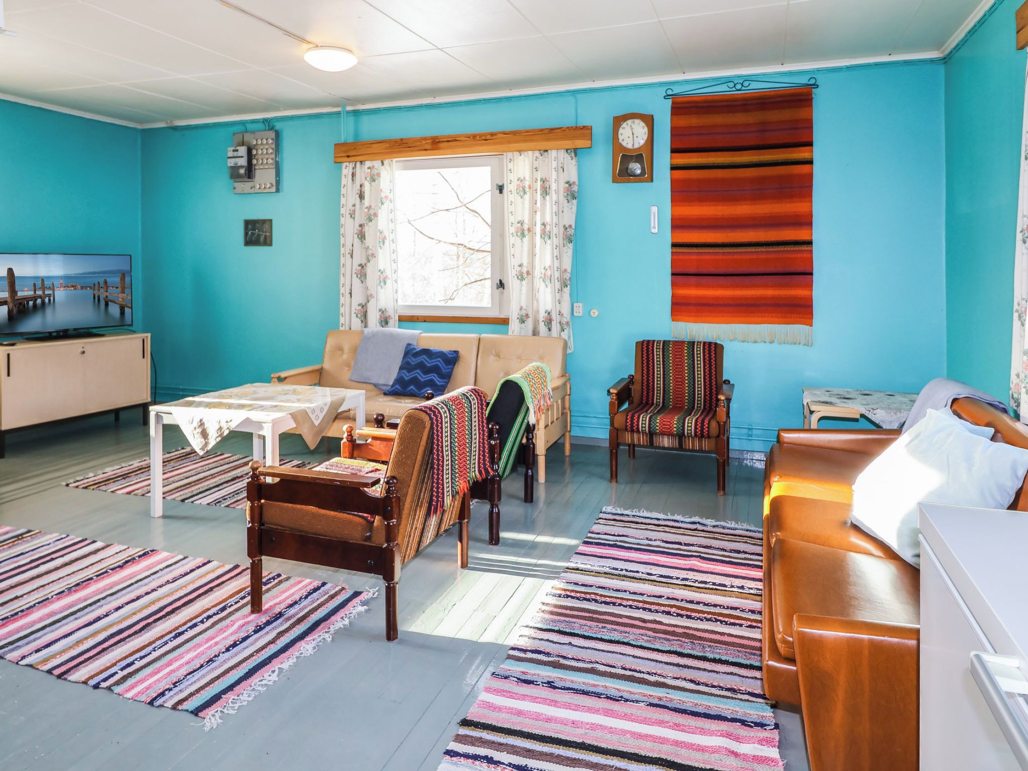 A room with a sofa, chairs, a small table, a television, and a window with curtains.