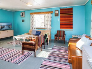 A room with a sofa, chairs, a small table, a television, and a window with curtains.