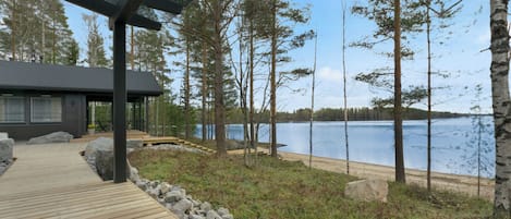 A wooden deck leading to a cabin with a view of a lake and trees.