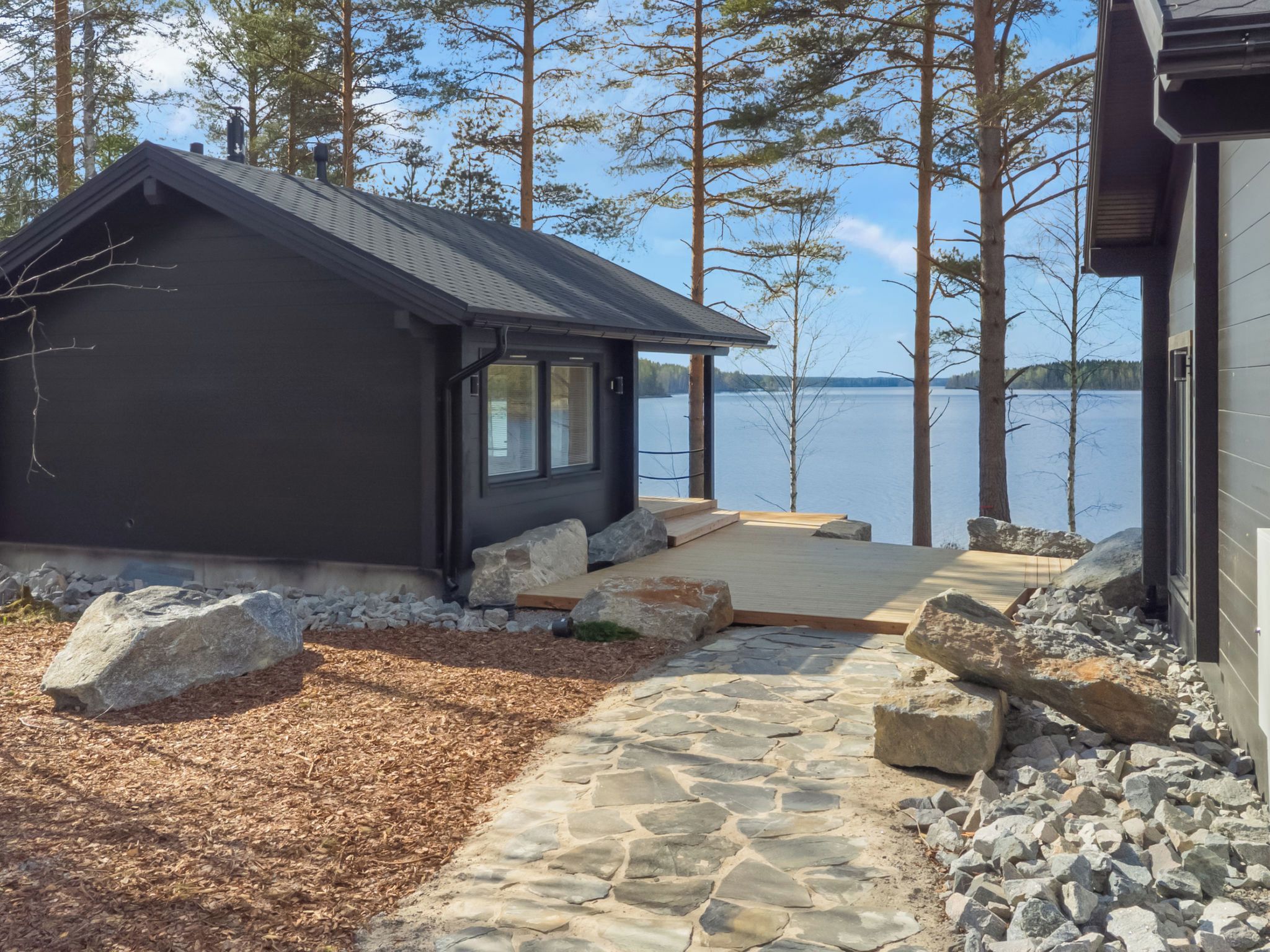 Una cabaña con un sendero de piedra que lleva a una terraza de madera con vista a un lago.