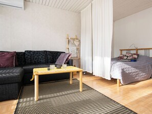 A modern living room with a sofa, a wooden coffee table, a bed with a quilt, and a wall-mounted rack with decorative items.