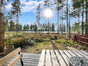 A wooden deck with a bench and a table, overlooking a forest and a body of water. - Joutiainen i 55 by Interhome (Hartola)