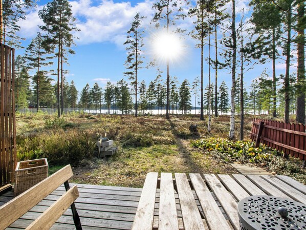 A wooden deck with a bench and a table, overlooking a forest and a body of water.