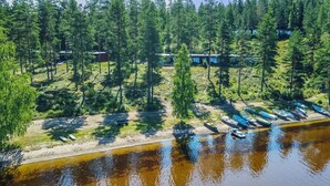 Vue aérienne d’une propriété au bord d’un lac, avec des chalets, un quai et une zone boisée.