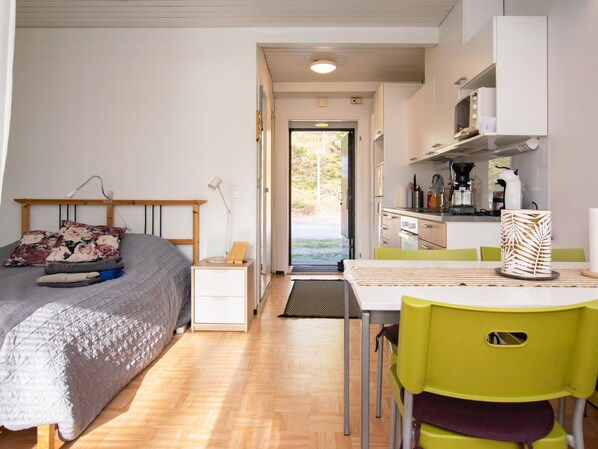 Un dormitorio pequeño con cama, mesita de noche y vista a una cocina por una puerta abierta.