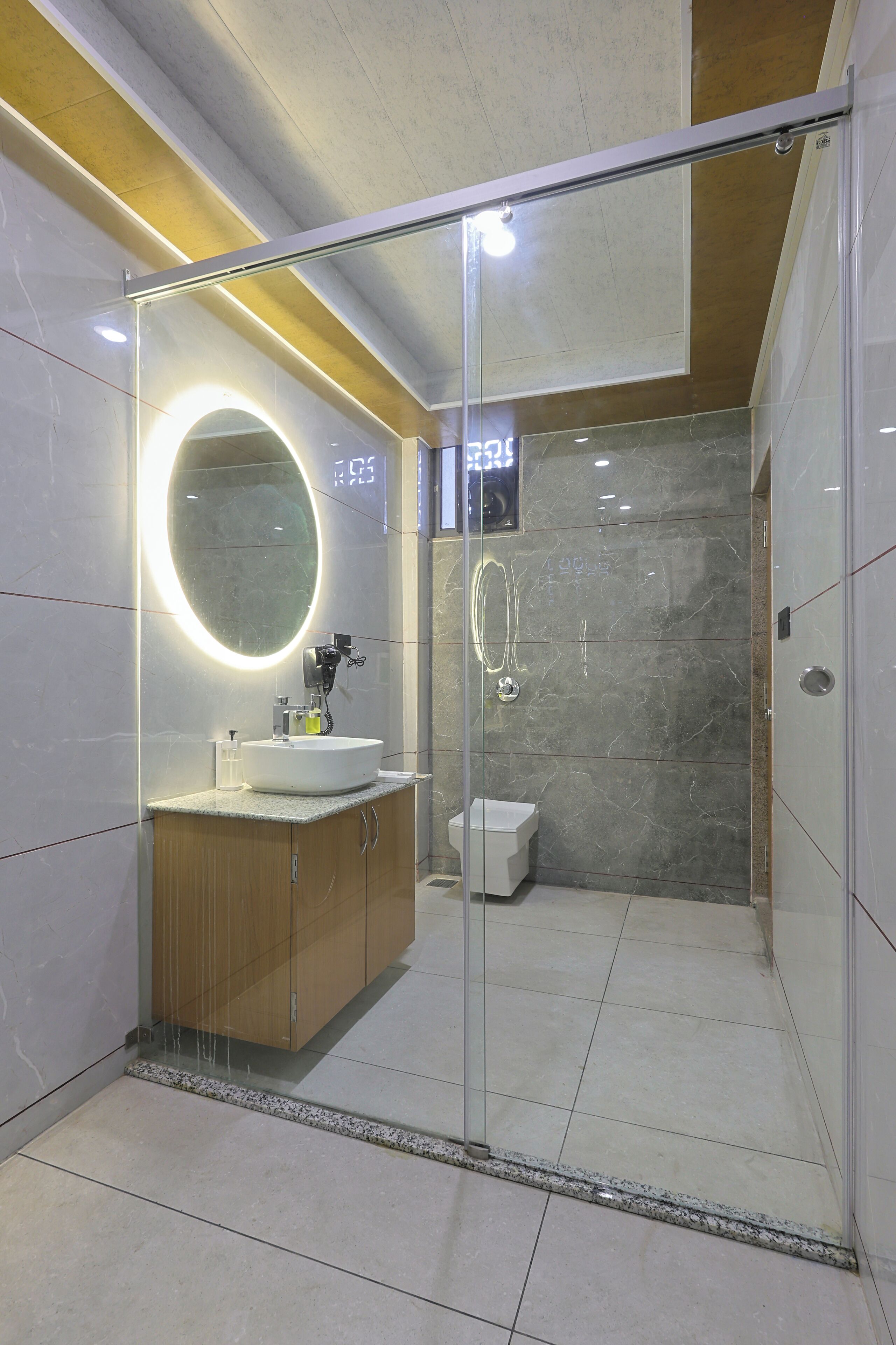 A modern bathroom with a glass-enclosed shower, a round mirror with lighting, and a white sink.