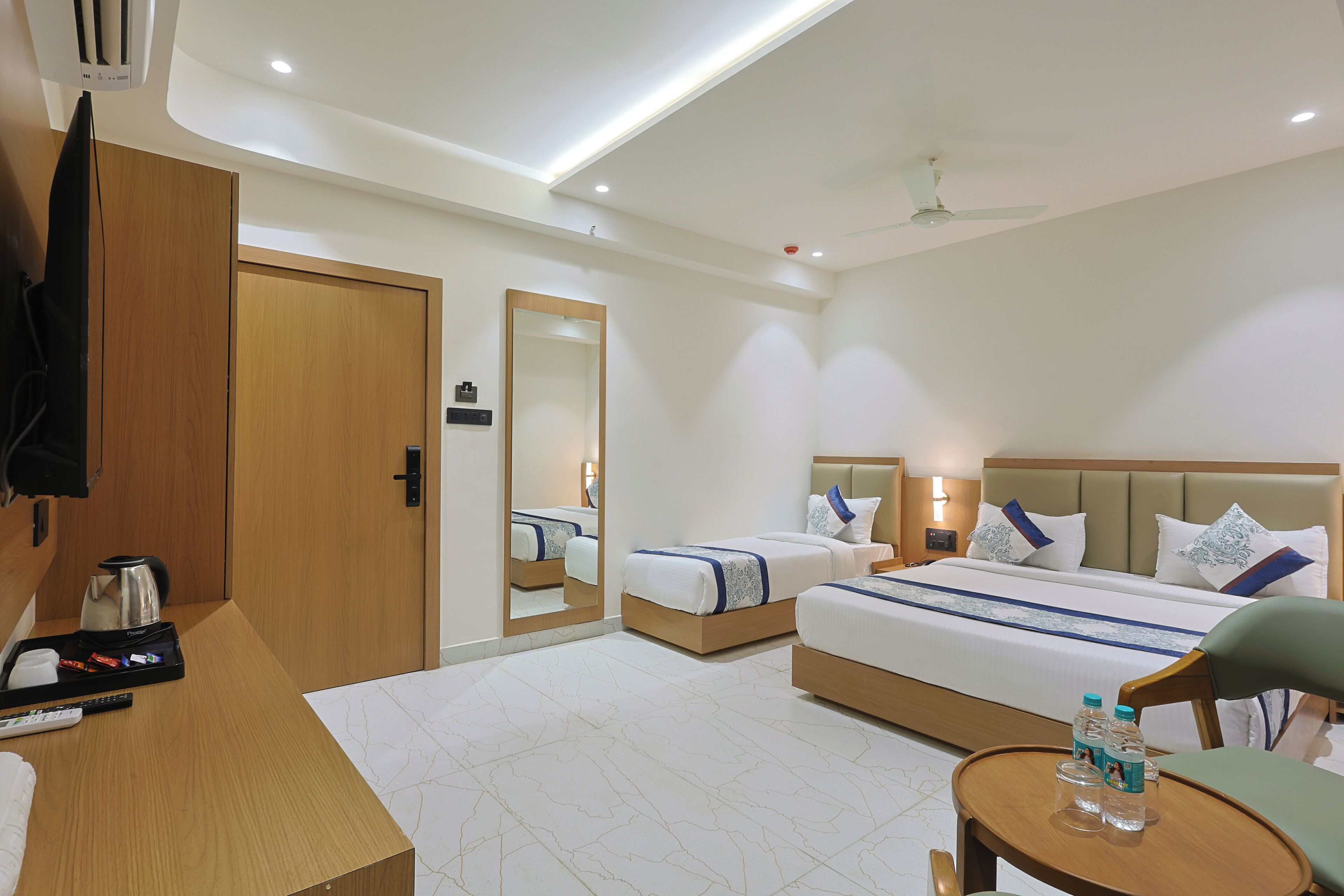 A hotel room with two beds, a wooden desk, a mirror, and a ceiling fan.
