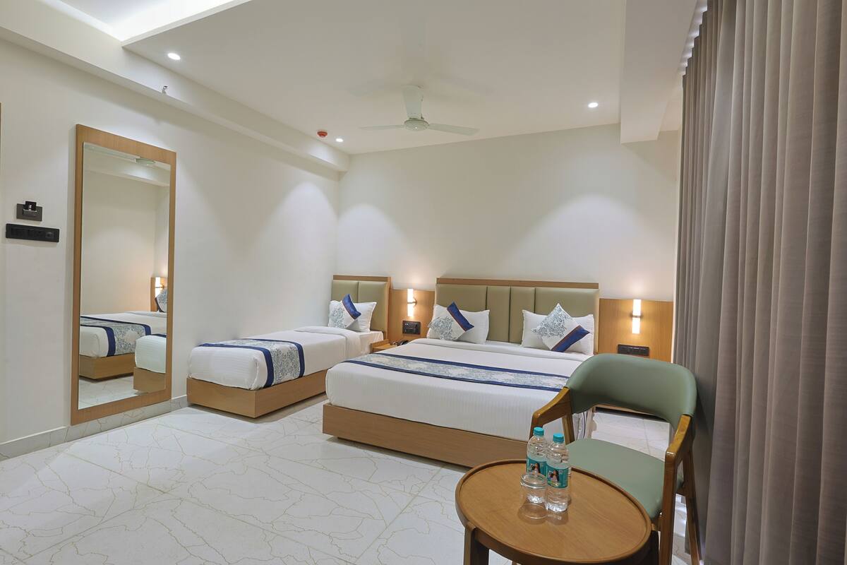 A hotel room with two beds, a round table with water bottles, a ceiling fan, and a large mirror.