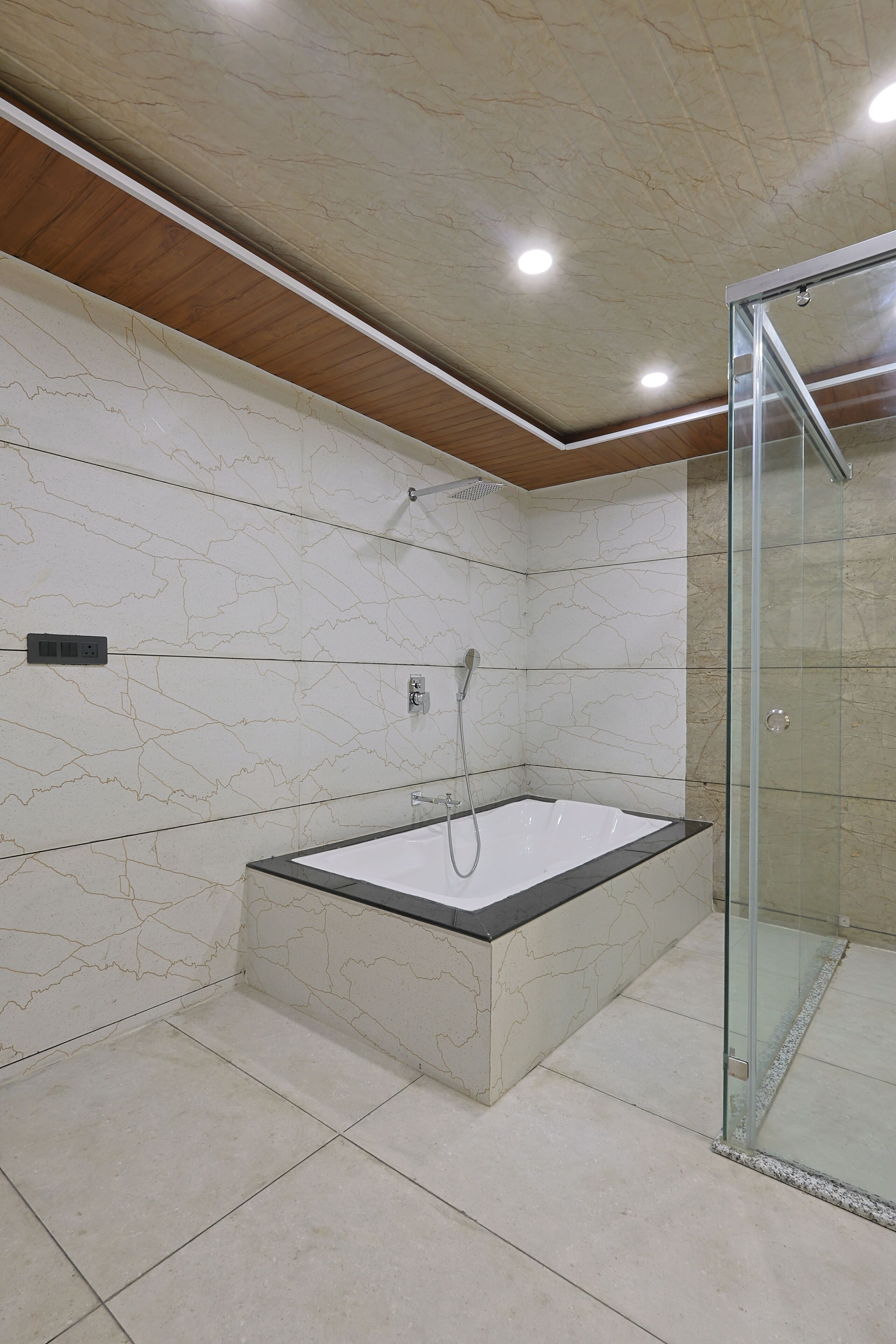 A modern bathroom with a glass-enclosed shower, a freestanding bathtub, and marble-patterned walls.