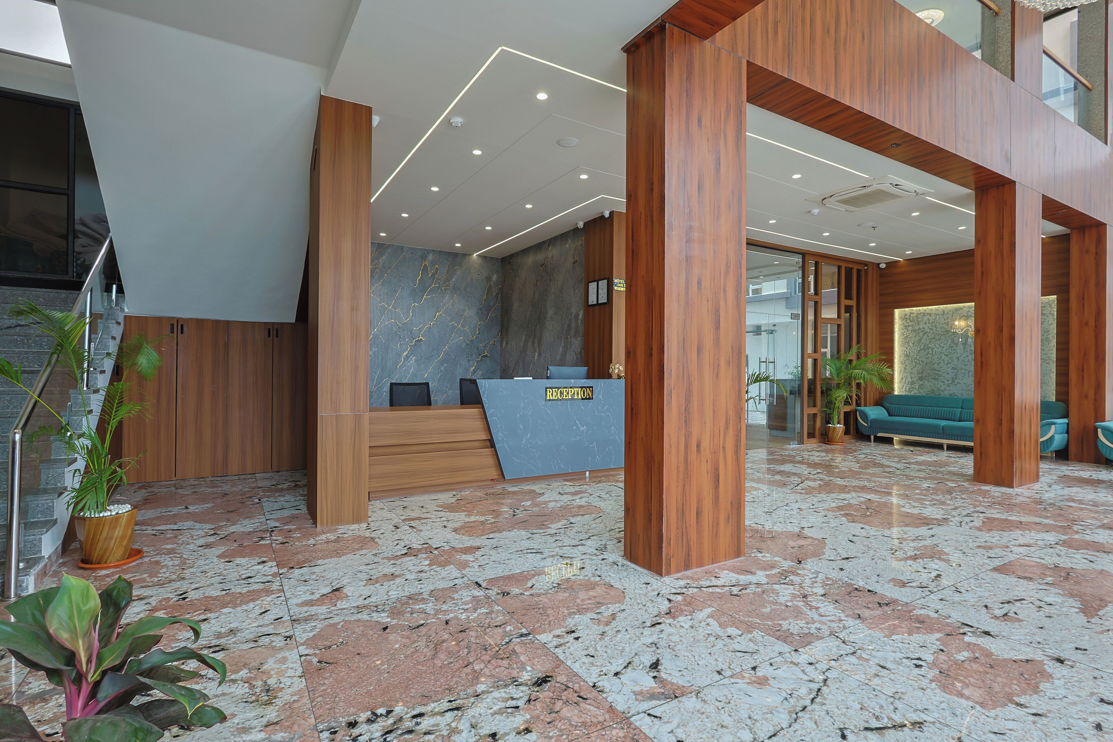 A modern reception area with a marble floor, wooden reception desk, and a green sofa in the background.