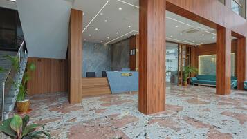 A modern reception area with a marble floor, wooden reception desk, and a green sofa in the background.