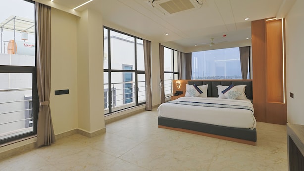 Quarto de hotel moderno com uma cama grande, mesa de cabeceira e vista da cidade através de amplas janelas.