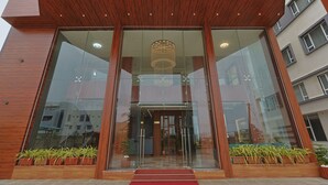 Entrada de um edifício moderno, com portas de vidro, lambris de madeira e plantas em vasos.