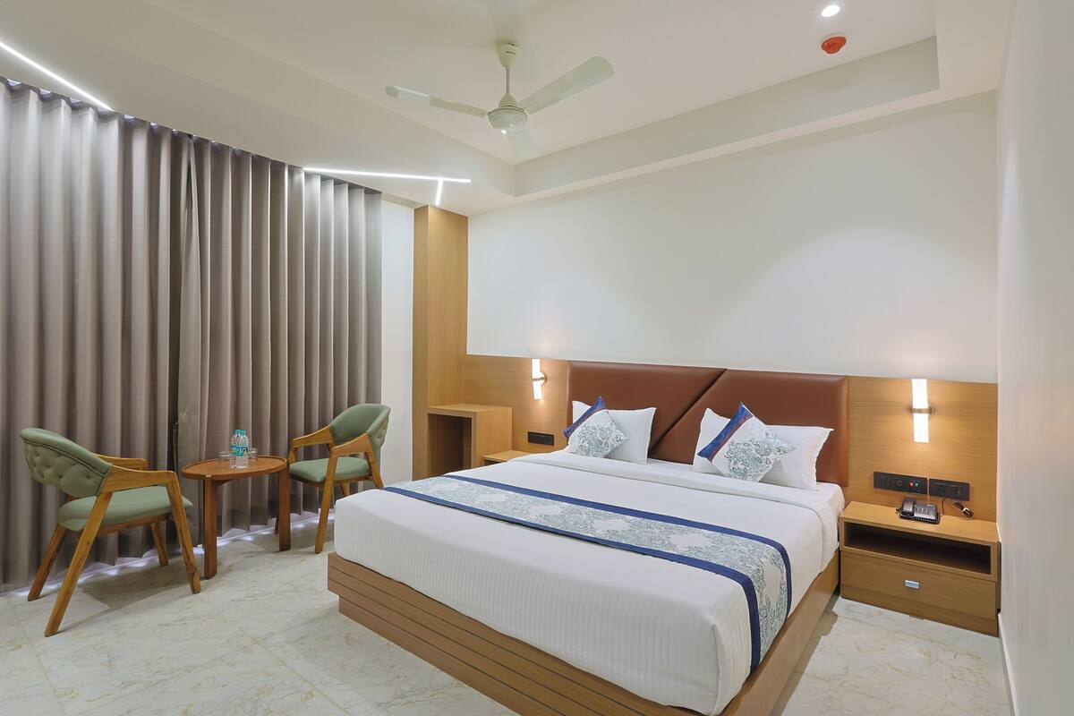 A hotel room with a large bed, two chairs, a small table, a ceiling fan, and a nightstand with a phone.