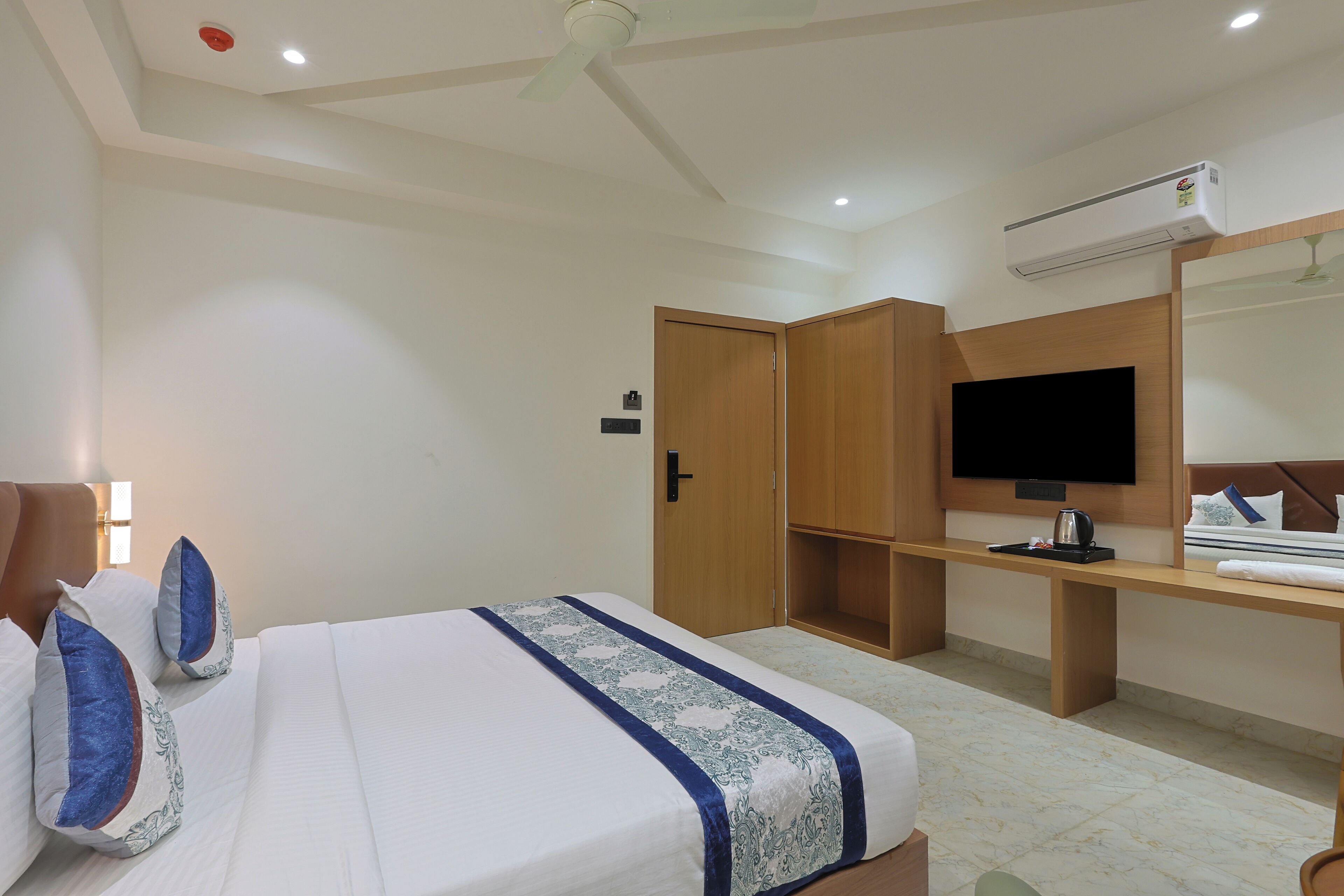 A hotel room with a bed, a desk, a TV, and an air conditioning unit.