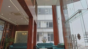 Um hall espaçoso com um lustre moderno, sofás verdes e piso de mármore.