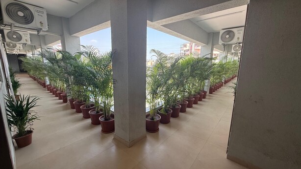 A corridor lined with potted plants, supported by concrete pillars, with ceiling fans and a view of buildings in the background. - Hotel Wow Inn  (Pune)