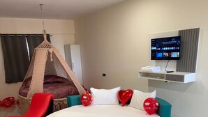 A modern bedroom with a circular bed, teal furniture, a hanging chair, and a TV on the wall. - Hotel Wow Inn  (Pune)