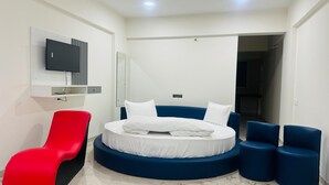 A modern bedroom with a round bed, a red chair, and blue ottomans. - Hotel Wow Inn  (Pune)