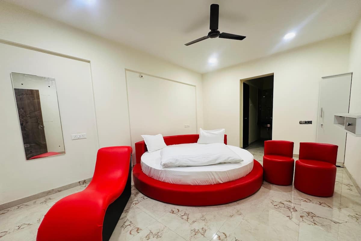 A modern bedroom with a circular bed, red seating, a ceiling fan, and a large mirror.
