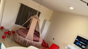A modern room with a circular bed, a hanging chair, a flat-screen TV, and teal chairs. - Hotel Wow Inn  (Pune)