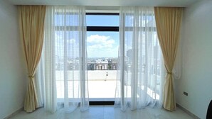 Una habitación con ventanas amplias, cortinas color beige y vistas a un paisaje urbano.