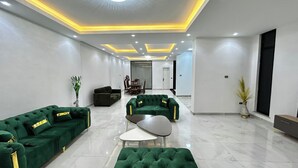 Amplia sala de estar con sofás verdes y una mesa de centro moderna, comedor con una mesa y sillas, y un pasillo que lleva a una puerta.