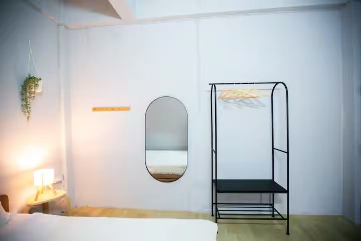A minimalistic room with a bed, a hanging plant, a round mirror, and a metal bunk bed.