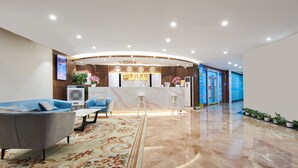 A hotel reception area with a marble counter, a reception desk, a blue sofa, and a floral carpet. - Meiyi Grand Hotel Shenzhen Huanggangcun (Shenzhen)