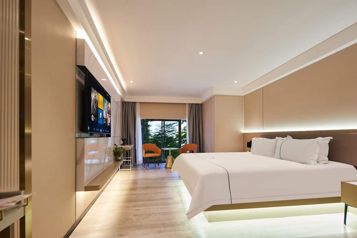 Quarto de hotel moderno com uma cama grande, televisão fixada na parede e um espaço de estar com cadeiras e uma mesa.