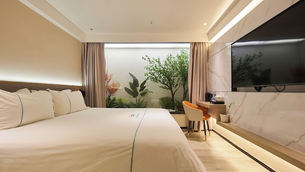 A modern hotel room with a large bed, a desk, and a TV mounted on the wall. - Meiyi Grand Hotel Shenzhen Huanggangcun (Shenzhen)