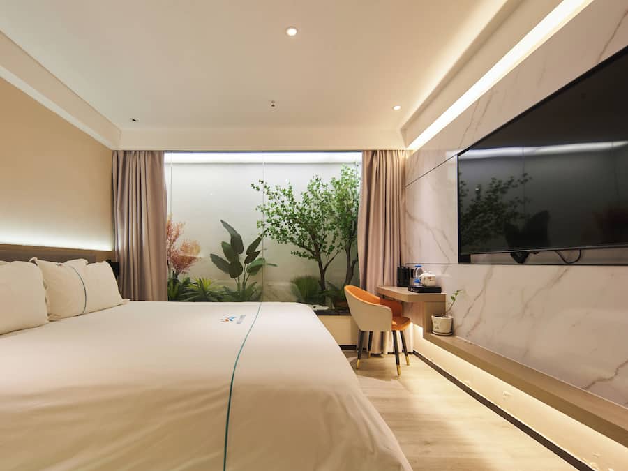 A modern hotel room with a large bed, a desk, and a TV mounted on the wall.