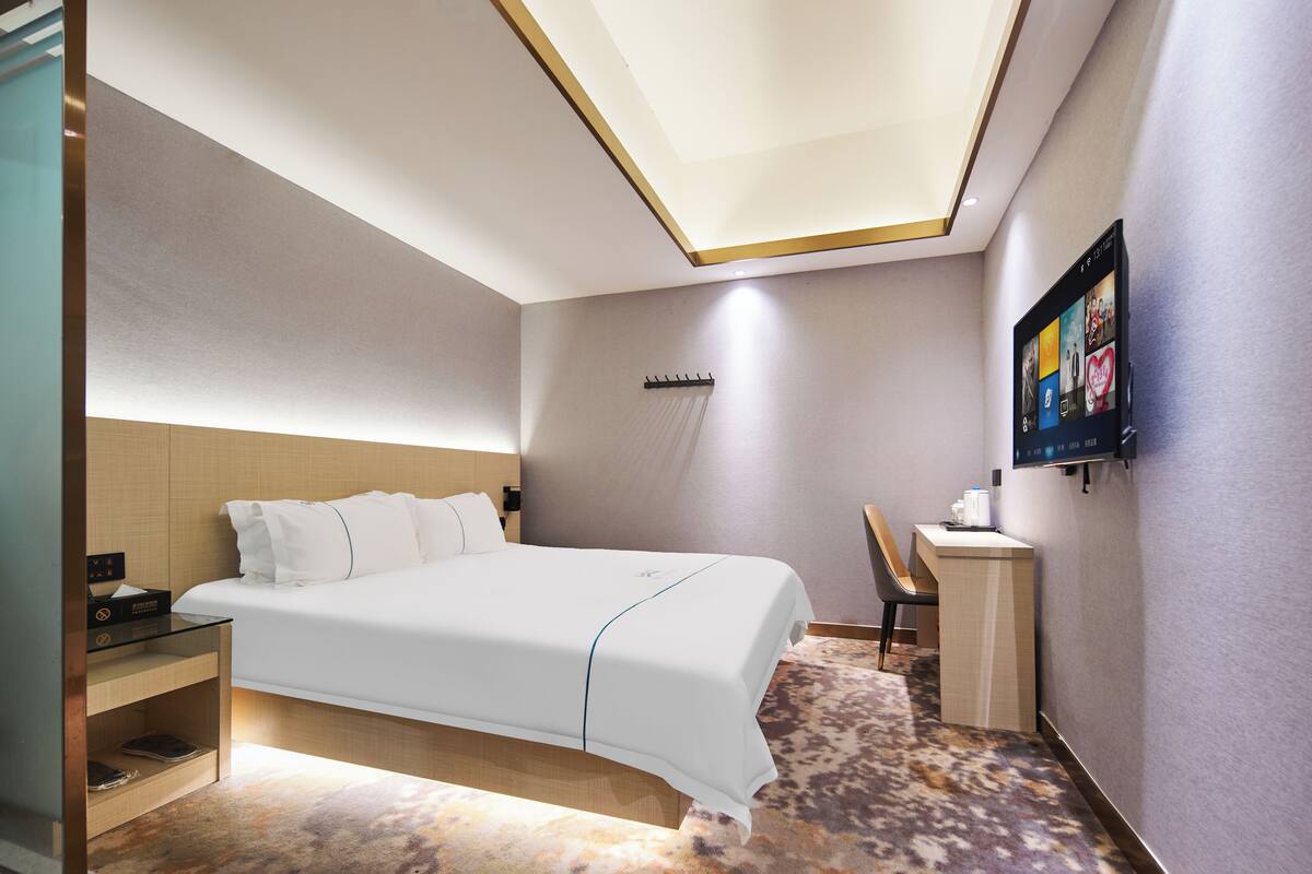 Quarto de hotel moderno com cama bem arrumada, escrivaninha e televisão na parede.