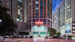 A hotel with a prominent red sign, surrounded by high-rise buildings and parked cars. - Meiyi Grand Hotel Shenzhen Huanggangcun (Shenzhen)